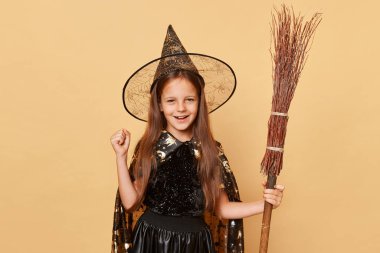 Cadı kostümü giymiş son derece mutlu bir kız elinde süpürgeyle cadılar bayramı arkaplanından izole edilmiş cadılar bayramı kutlaması yumruğunu sıkmış Cadılar Bayramı partisini kutluyor..