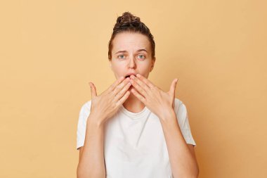 Şok olmuş beyaz tişört giyen korkmuş kadın saçlarını yıkar. Kafasında şampuan köpüğü ile ayakta durur. Bej arka planda izole edilmiş..