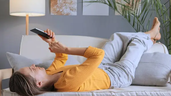 Wanita Cantik Yang Santai Terletak Sofa Rumah Menggunakan Ponsel Membaca — Stok Foto