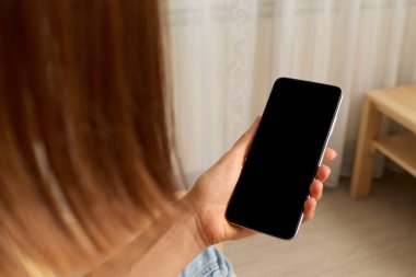 Mobil bağlantı. Dijital bir model. Sanal toplantı. El aydınlatma odasının iç tarafında elinde boş ekranlı akıllı telefon tutan tanınmayan kahverengi saçlı kadın..