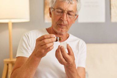 Sağlıksız, gri saçlı, günlük beyaz tişörtler giyen, oturma odasındaki kanepede oturan ilaç almak için bardaktan damlalar koyan, kendini kötü hisseden, haplara ihtiyacı olan son sınıf öğrencisi...