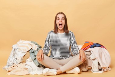 Çizgili tişört giyen son derece çılgın bir kadın yerde oturuyor. Etrafı darmadağınık kıyafetlerle çevrili. Çığlık çığlığa..