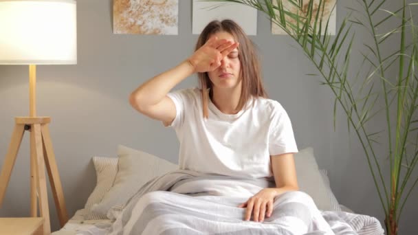 疲れた眠っている女性は 睡眠不足のために頭痛を抱えている仕事のために遅れている悪い気分で目を覚ます間 彼女の手で白いTシャツをこすっている — ストック動画