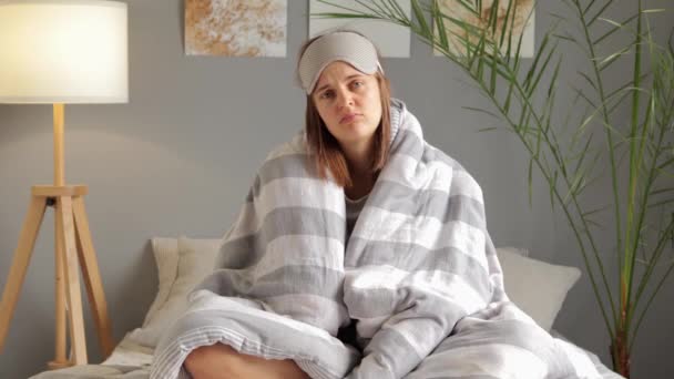 ベッドの上のストライプの毛布に包まれた悪い外観の不幸な女性は落ち込んで起き上がり 眠れない夜の後の朝の疲労を強調するエネルギーがありません — ストック動画
