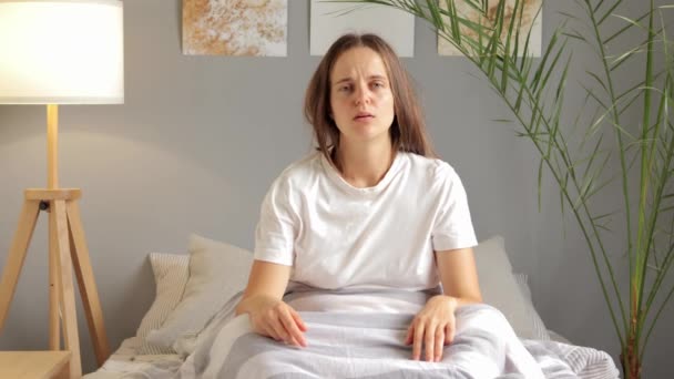 疲惫的女人穿着白色T恤 困倦地打呵欠 醒来后又躺在床上 需要更多的时间睡觉 — 图库视频影像