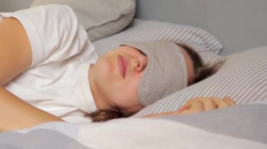 Güzel, uykucu, göz bağı takan, gülümseyen, tembel bir hafta sonu uykusunda uyuyan bir kadın. Evde yatakta uzanmış uykusuzluğun tadını çıkarıyor..