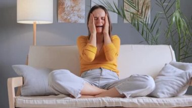 Mutsuz, stresli, beyaz kadın depresyonda. Kanepede oturuyor. Üzgün kadın, evde yalnız başına ağlamakta zorlanıyor..