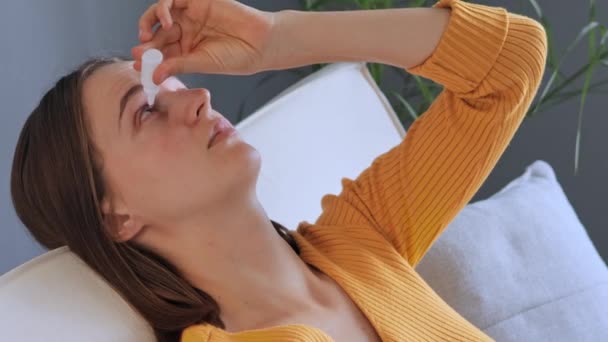 医学的な目を使用している若い白人女性は 乾燥した眼症候群に苦しんでいるか 自宅で眼科疾患を治癒し 自宅の内装で目を輝かせている — ストック動画