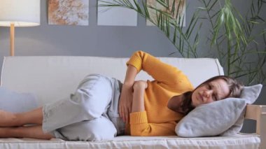 Mide rahatsızlığı çeken beyaz bir kadın avuçlarını karnında tutar. Aybaşı krampları olur. Günlük sarı gömlek giyer, bozuk yemek yedikten sonra kot pantolon sancısı çeker..