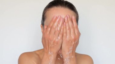 Dişi güzellik ve cilt bakımı. Temiz ve taze deri. Kaplıcada cilt bakımı rutini. Doğal yüz temizleme. Hijyen ve cilt sağlığı. Çıplak omuzlu, yüzünü yıkayan, gri arka planda yalnız bir kadın.