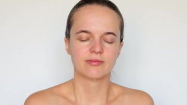 Serinletici su sıçraması. Kadınlık ve saflık. Refah ve zindelik. Saf olmayan şeyleri nazikçe ortadan kaldırmak. Gri arka planda çıplak esmer kadın yüzünü yıkıyor..