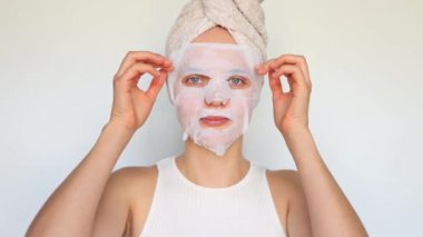 Günlük kişisel bakım rutini. Dermatoloji ve cilt bakımı. Sağlık ve refah. Beyaz arka planda izole edilmiş beyaz tenli ve parlayan yüzler için beyaz kadın kozmetik doku maskesi takıyor..