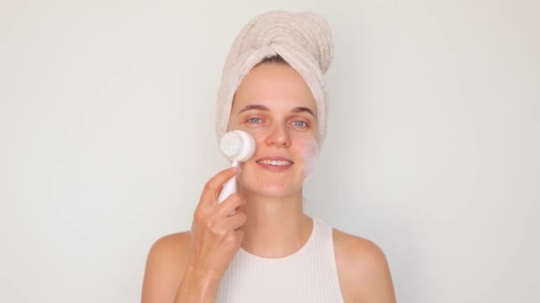 卫生和化妆品学 润肤的日常护理 新鲜而快乐的脸 快乐的成年女子在洗头脸上裹着毛巾 用按摩器清洗被白色背景隔离的皮肤 — 图库视频影像