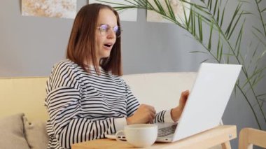 Web serbest çalışanı. Girişimci teknolojisi. Bilgisayar eğitimi. Neşeli, başarılı, günlük kıyafetler giyen ve gözlüklü bir kadın. Evde çalışıyor. İyi iş çıkarmasını kutluyor, yumruklarını sıkıyor..