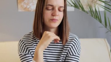 Panik atak. Stres yüzünden depresyonda. Korkudan canı sıkkın. Gergin endişe. Depresif bir duygu. Dehşet verici korku. Evinde oturan, çizgili gömlek giyen endişeli ve üzgün, koyu renk saçlı kadın..