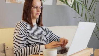 Elektronik öğrenim dijital. Siber uzay girişimcisi çevrimiçi. Aşırı çalışan kahverengi saçlı, günlük kıyafetler ve gözlük takan internetten çalışan ev içinde yorgun ve ağrılı bir boyun hisseden bir kadın..