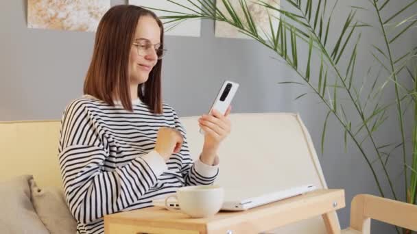 노트북과 커피와 소파에 캐주얼 셔츠를 그녀의 스마트 인터넷 페이지와 네트워크 — 비디오