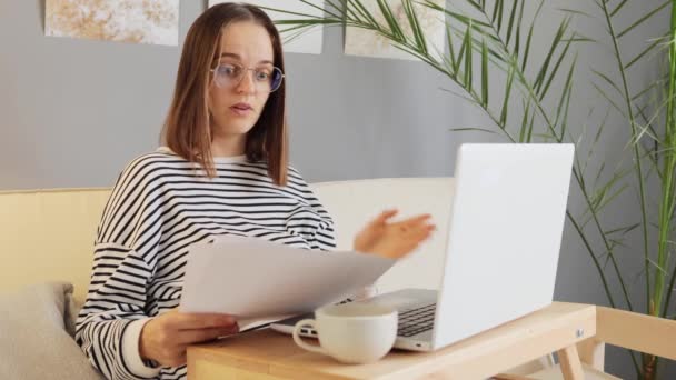 穿着休闲装和眼镜在家里工作的棕色头发女人在网上和文书工作中阅读文件 试图发现错误时感到惊讶 — 图库视频影像