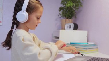 Çevrimiçi dersler. İnteraktif çevrimiçi öğrenme deneyimi. Beyaz gömlekli, güzel, genç bir kız, bir dizüstü bilgisayarın önünde masasında oturmuş, dikkatle online bir ders izliyor..