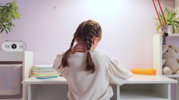 疲れた疲れた女の子は 痛みを伴う背中の痛みをマッサージする家庭の仕事をするテーブルに座って白いセーターを身に着けている — ストック動画