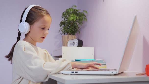 リモート宿題が助けになる デジタル学習ツール ホームスクーリングオプション 子供のためのバーチャル教室 フロントラップトップのデスクに座って白いシャツを着用したピグテールとチャーミングな少女 — ストック動画