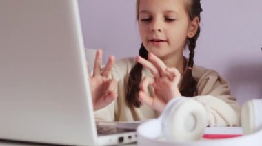 Çocukların çevrimiçi kursları. Temel e-öğrenme. Çevrimiçi dersler başlıyor. Siyah saçlı, atkuyruklu, tişörtlü, dizüstü bilgisayarının önünde oturmuş parmaklarıyla sayarak online matematik dersi alan küçük bir kız..