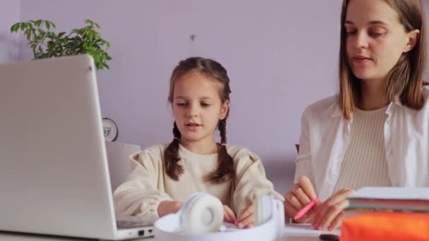 坐在笔记本电脑前的漂亮的小女孩在完成作业时得到了妈妈的帮助 妈妈承担了老师的角色 并向可爱的小学生解释了 — 图库视频影像