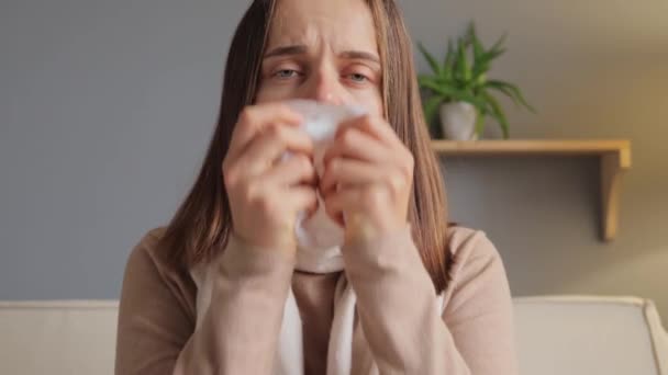 インフルエンザ症状 病気の女性 季節性アレルギーについて 不健康な悲しい茶色の毛髪の女性のコビド感染症は 家庭内インテリアで鼻水を患っているティッシュで鼻を吹く — ストック動画