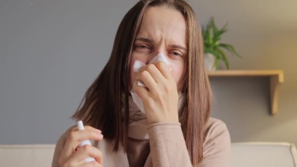 ナスラル灌漑 ナスラベッジ 不健康な若い女性は鼻のスパイを使用して 彼女の鼻の鼻と風邪を不快な感情から飛ぶスカーフに包まれてソファーに座って治療します — ストック動画