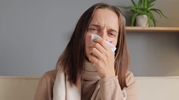 保健和保险 年轻的白种人女人坐在沙发上 戴着口罩 带着感冒和高烧 脸上带着不舒服的表情 — 图库视频影像