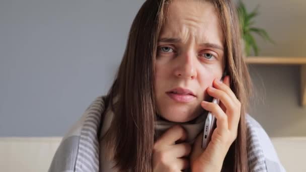 医者とのスマートフォンで話す毛布で包まれた茶色の髪の不健康な病気の女性は ウイルス病がうまくいかないように見える電話相談を持っています — ストック動画