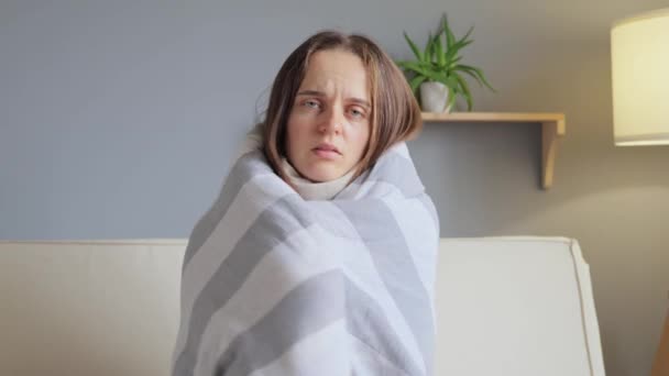 Virus infection. Sick woman. Home healthcare. Bad feeling brown haired girl wrapped plaid sitting sofa suffering from catching cold in home interior.