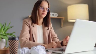 Modern çalışma alanı. Profesyonel bir iş. Yorgun, kahverengi saçlı, resmi tarz ceket giyen, dizüstü bilgisayarda çalışan, iş yerindeki ödevini bitirmesi gereken bir ofis çalışanı..