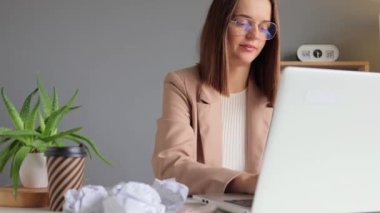 Laptop işi. Çalışma süreci. Etkileyici bir çalışma alanı. Modern teknoloji. Çekici, kahverengi saçlı, resmi stil ceket giyen bir kadın modern ışık ofisinde dizüstü bilgisayarla internet üzerinde çalışıyor..