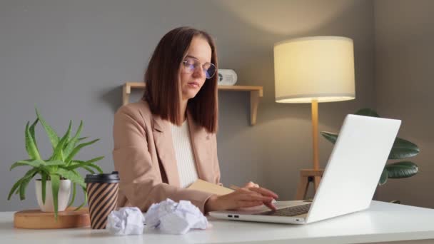 在现代公司的办公室里 穿着米黄色夹克的聪明聪明的棕色头发女人坐在自己的工作岗位上 用笔记本电脑处理文档和在线数据库 — 图库视频影像