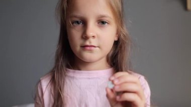 Hasta çocuk. Sağlık sigortası. Küçük ilaç. Kahverengi saçlı küçük kız elinde hapla çocuk hastalıklarını tedavi ederken kameraya bakıyor..