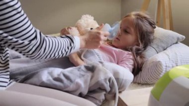 Küçük bir kız nebulizörle güzel bir anneyle nefes alıp veriyor. Hasta bir anneye, soğuk algınlığı ve nezle olan kızına nebuliser sprey soluması için yardım ediyor..