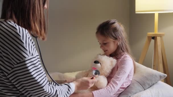 母亲和小女儿在家当医生 而孩子生病休假时 使用听诊器听泰迪熊在孩子感冒时玩乐 — 图库视频影像