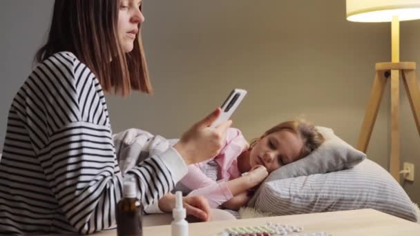 黑发女子在网上与医生谈论女儿发烧 摸小孩额头 测量体温 询问专业治疗流感的方法 — 图库视频影像