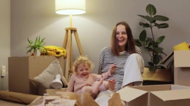 Neşeli Kafkas anne ve bebek kızı taşınıyor. Karton kutularla dolu yeni bir daire. Mutlu bir şekilde gülerek taşınıyorlar..