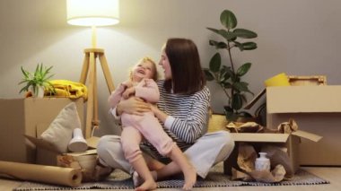 Yeni bir ev için ipotek. Kutuları birlikte paketliyoruz. Kafkasyalı anne ve kız bebek yeni bir eve taşınıyor. Karton kutularla dolu. Aile kucaklaşıyor ve sevgisini ifade ediyor..