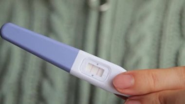 İki kırmızı çizgili, hızlı ve pozitif hamilelik testi yapan kimliği belirsiz bir kadın hamile olduğunu doğruladı. Bu da kameraya örgü gömlek giydiğini gösteriyor..