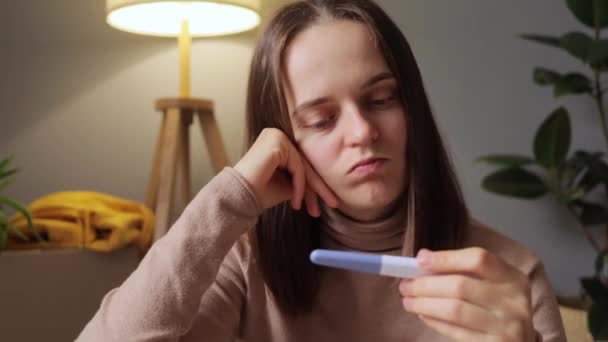 自宅に座って不満な表情で結果を見ている妊娠テストをしたがっかりした女性は 将来の母親は親になる準備ができていないか 1つのストリップに動揺している — ストック動画