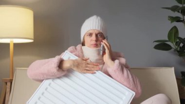 Soğuk kadın, kürk manto ve kep giyip evde oturmuş ısıtıcıya sarılıyor, servis sırasında konuşuyor ve merkezi ısıtma sistemini çalıştırıp çalıştırmadığını soruyor..