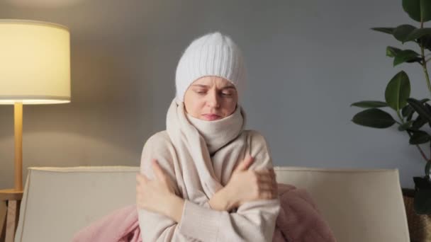穿着外套 头戴帽子的身体不舒服的女人坐在冰冷的客厅里 家里没有暖气 不健康的年轻女人在家里因寒冷而挣扎着冻僵 — 图库视频影像