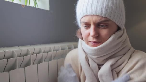 在寒冷的冬日里 穿着帽衫 头戴围巾 头戴手套 坐在电池旁边的冷冰冰的女人在家里被冻住了 没有中央暖气 她的身体也在家里受热 — 图库视频影像