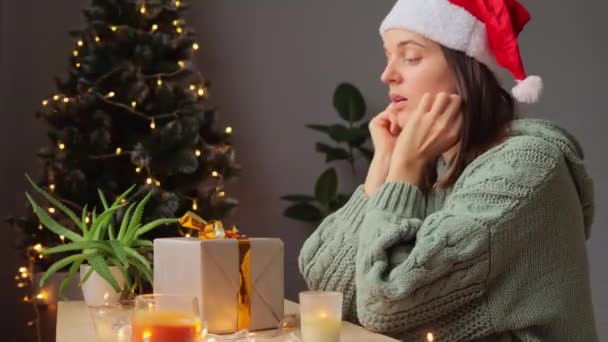 女人看着圣诞礼物 脸上挂着悲伤而不高兴的表情 准备在家庆祝 背景上装饰着圣诞树 — 图库视频影像