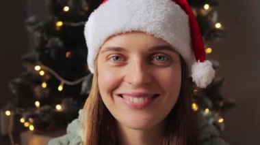 Noel Baba şapkası takan mutlu genç bayanın selfie pov çekerek yeni yıl tatilini kutlarken kameraya gülümseyerek mutluluğu ifade ettiği yakın plan..
