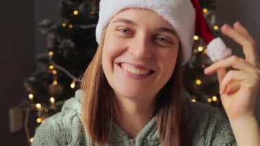 Çekici, mutlu, çekici bir kadın Noel Baba şapkası takıyor. Mutlu yıllar tatili kutluyor. Kameraya gülümsüyor ve neşeli bir ruh hali içinde..