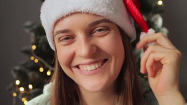 Noel Baba şapkası takan yakın plan kadın mutlu bir gülümsemeyle kameraya bakıyor. Yeni yılı kutluyor. Sosyal ağı için neşeli bir ruh hali videosunda..